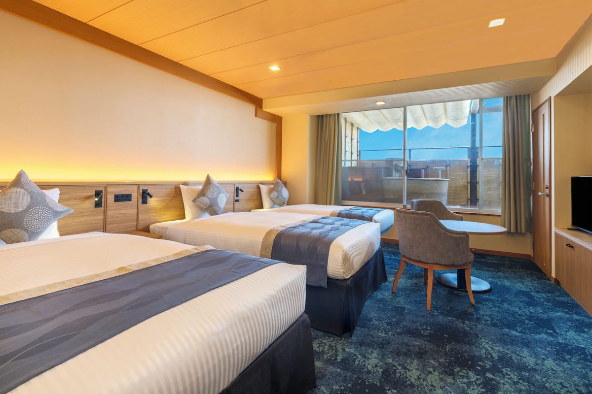A hotel room with two beds, a desk, a chair, and a large window with a view.