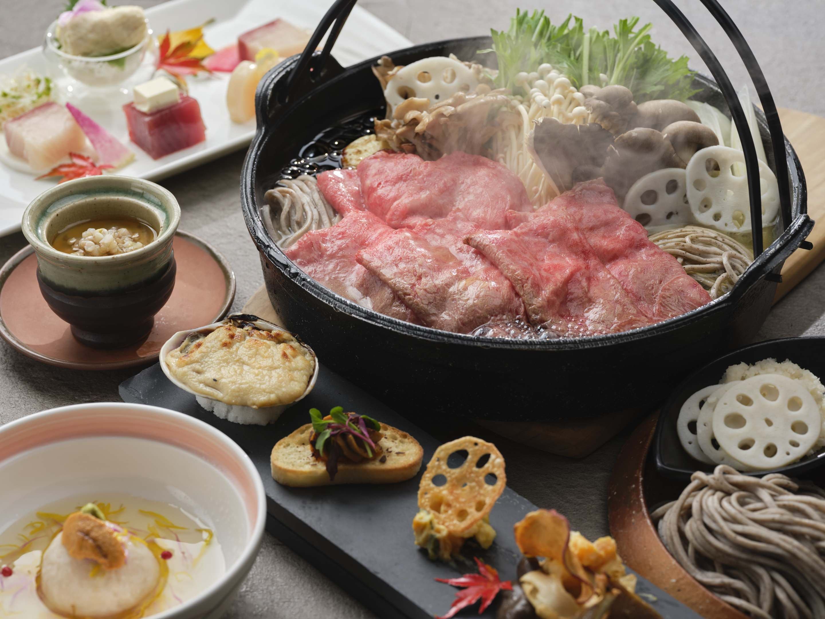 A hot pot with various meats and vegetables, accompanied by side dishes and condiments.