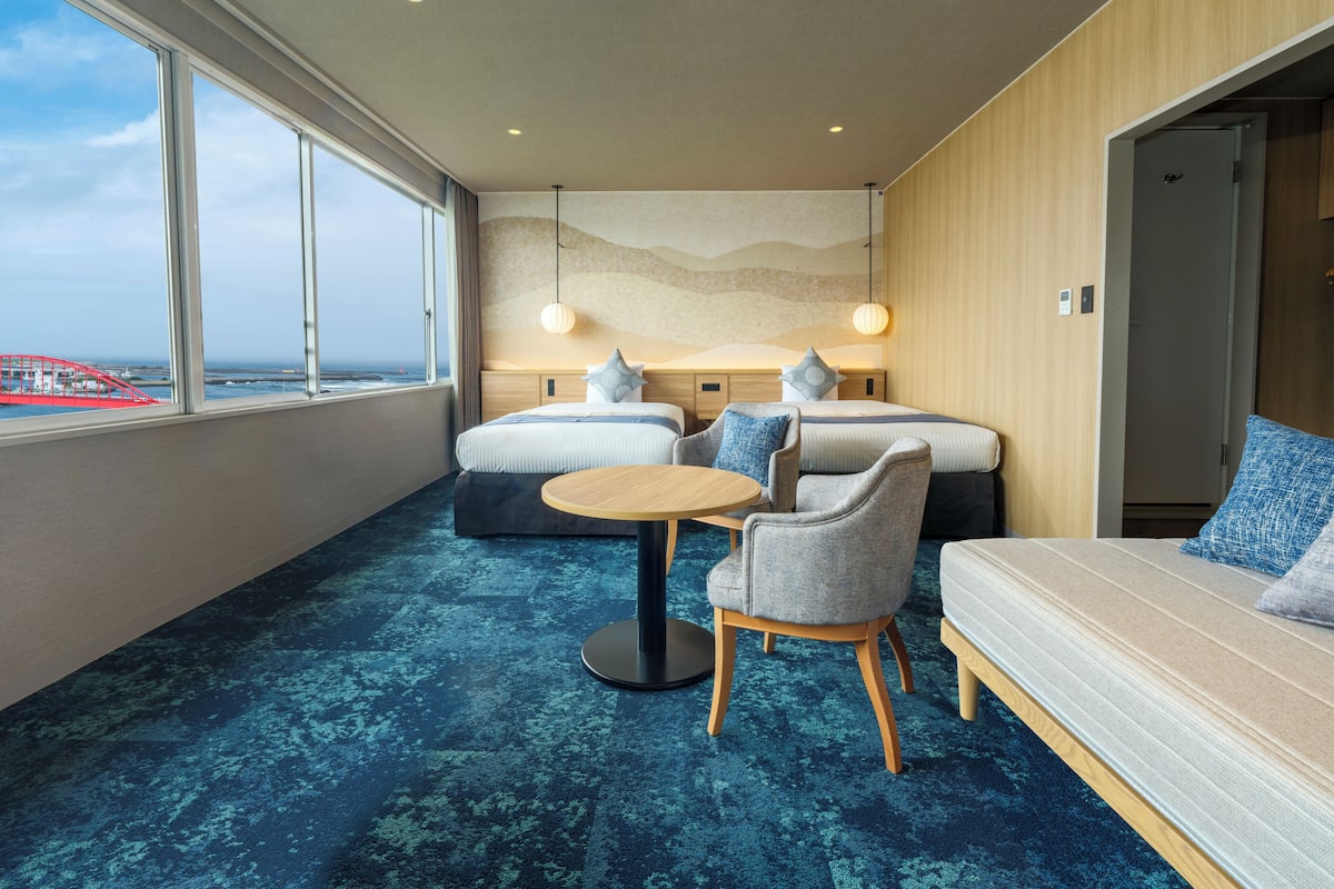 A modern hotel room with a large window, a round table, two sofas, and a bed.
