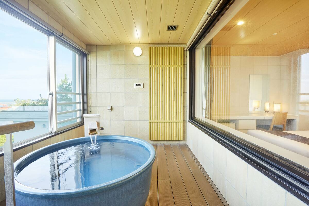 A modern bathroom with a large bathtub, a wooden floor, and a view of the outside.