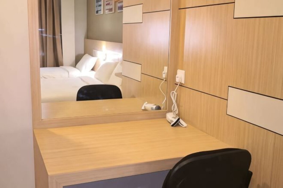 A hotel room with a wooden desk, a mirror, a bed with white linens, and a wall-mounted phone.