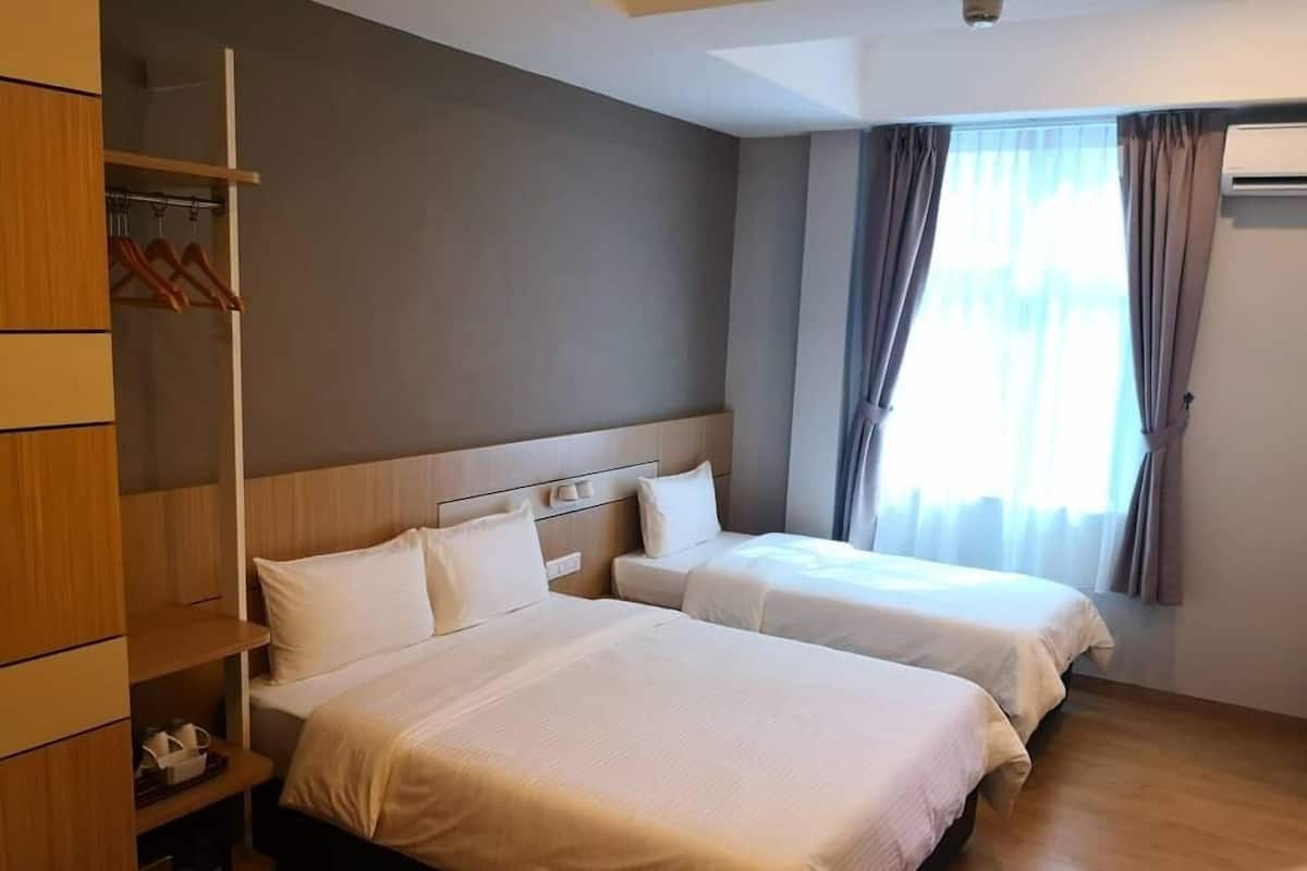 Quarto de hotel com duas camas, um guarda-roupa de madeira e uma janela com cortinas.