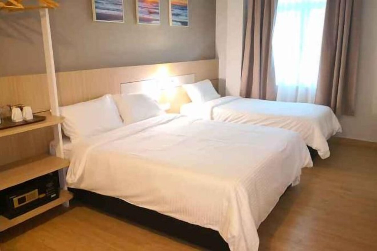 Ein Hotelzimmer mit zwei Betten, einem Nachttisch, einer Lampe und einem Fenster mit Vorhängen.