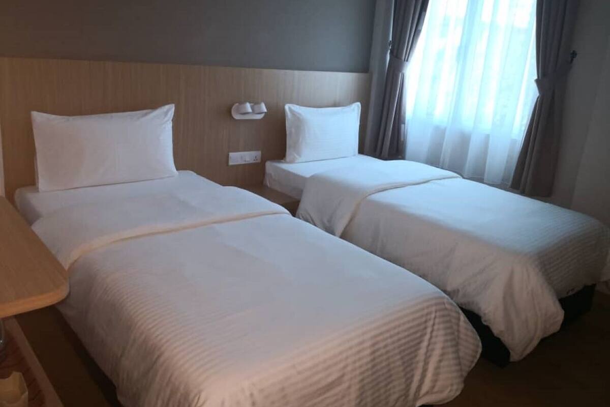 Quarto de hotel com duas camas de solteiro, cabeceira de madeira, mesa de cabeceira e janela com cortinas.