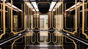A luxurious hotel lobby with a reflective black floor, gold-framed glass doors, and a central elevator. - Forestar (Seoul)
