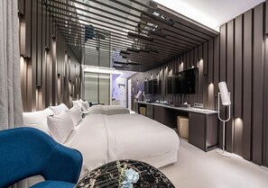 A modern hotel room with a large bed, a desk, a TV, and a seating area.