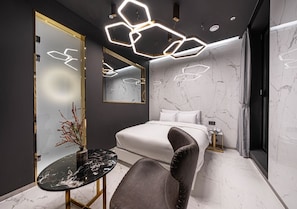 A modern bedroom with a bed, a vanity with a mirror, a small table, and a chair.