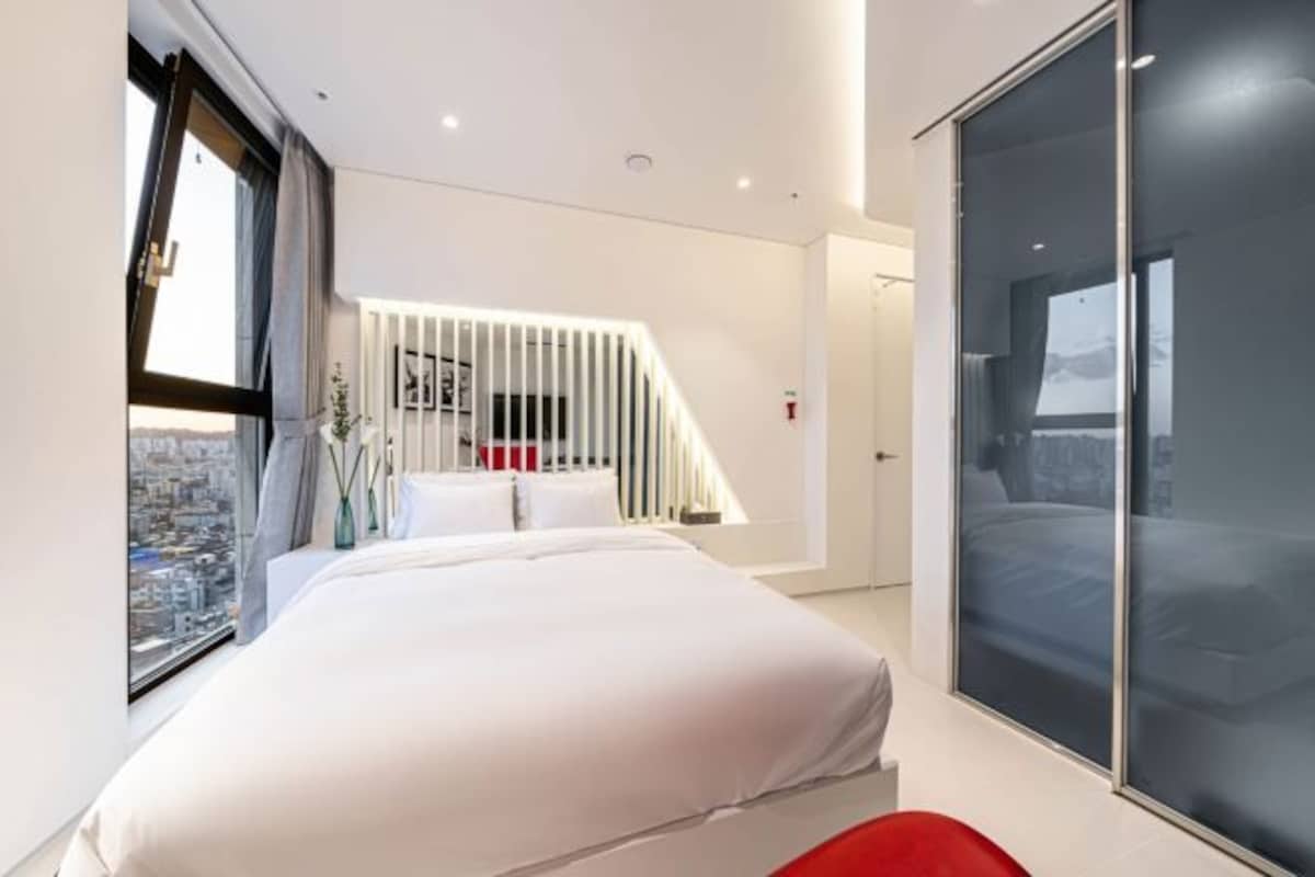 A modern bedroom with a large bed, a sliding glass door, and a view of the city.