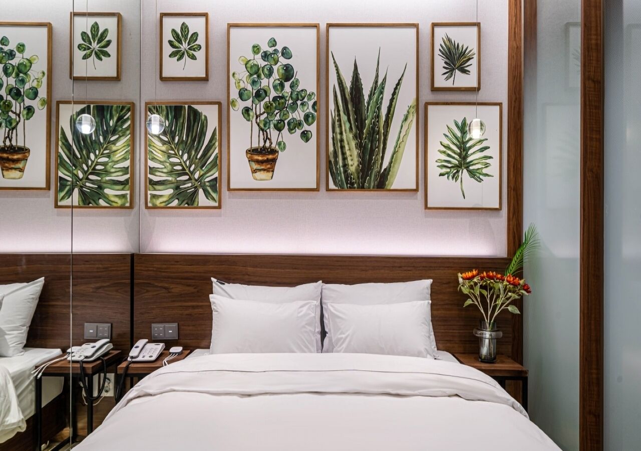 A hotel room with a large bed, a wooden headboard, a bedside table with a phone, and framed botanical artwork on the wall.