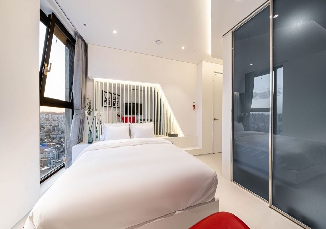 A modern bedroom with a large bed, a city view, a staircase, and a sliding glass door.