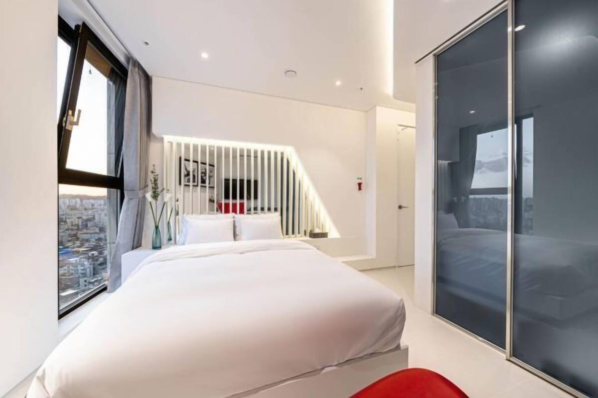 A modern bedroom with a large bed, a sliding glass door, and a view of the city.