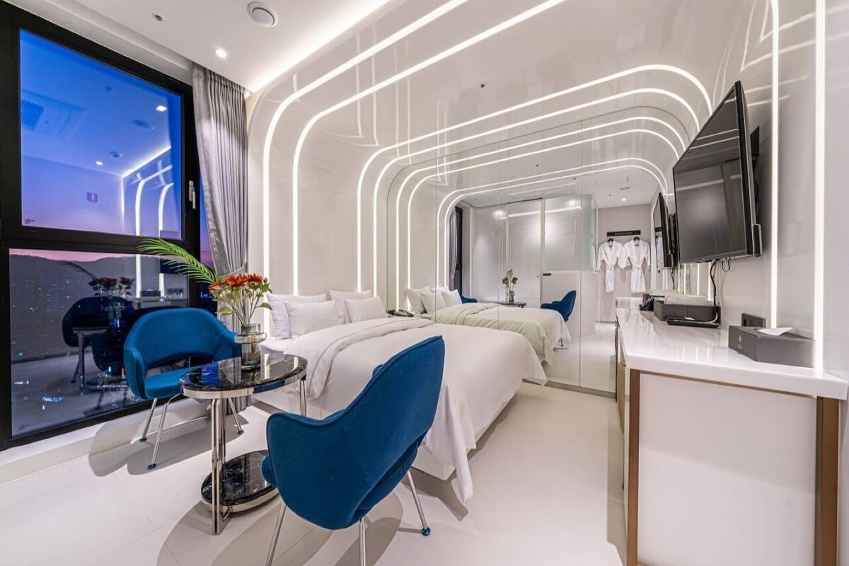 A modern hotel room with a large bed, a desk, a chair, and a TV.