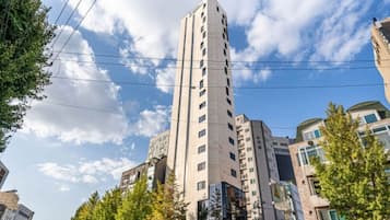 Ein hohes, modernes Gebäude mit mehreren Stockwerken, umgeben von Bäumen und anderen Gebäuden.