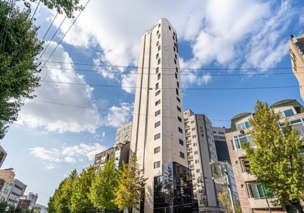 A tall, modern building with multiple floors, surrounded by trees and other buildings.