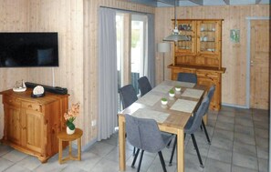 A dining area with a wooden table, chairs, a television, a cabinet with glass doors, and a small side table with a plant.