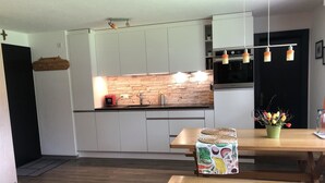 Eine moderne Küche mit weißen Schränken, einer Steinwandverkleidung und einem Essbereich mit Holztischen und -bänken.
