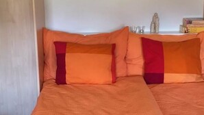 Ein Schlafzimmer mit einem Bett, das mit orangefarbener Bettwäsche bezogen ist, einem hölzernen Kopfteil und einem kleinen Tisch mit Büchern und einer Figur.