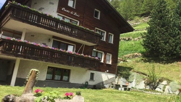 Ein mehrstöckiges Gebäude mit Balkonen, umgeben von Grünflächen und einer Berglandschaft.