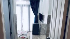 A hallway leading to a bedroom with a bed, a small refrigerator, and a window with curtains. - Song Huong House (Ho Chi Minh City)