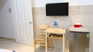 A compact kitchenette with a refrigerator, a wooden table, a chair, a television mounted on the wall, and a door. - Song Huong House (Ho Chi Minh City)