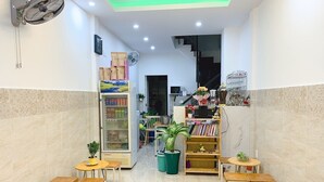 A cafe with wooden tables and chairs, a refrigerator stocked with beverages, and a bookshelf with books and decorative items. - Song Huong House (Ho Chi Minh City)
