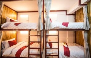 Ein Zimmer mit vier Etagenbetten, jeweils mit Holzrahmen und weißer Bettwäsche. Eine Leiter verbindet die Betten.