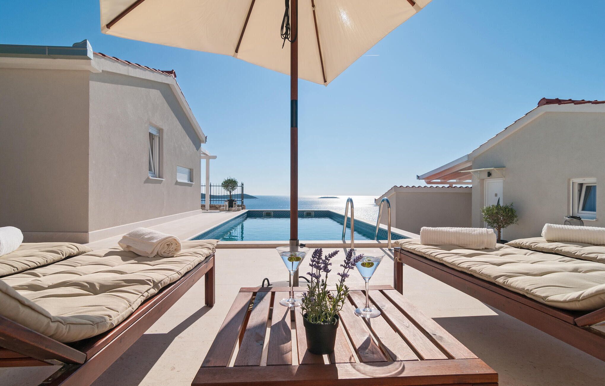 A poolside area with two sunbeds and a table with drinks and flowers, overlooking a clear blue sea.