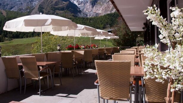 An outdoor seating area with wicker chairs and white umbrellas, overlooking a mountainous landscape.