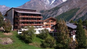 A multi-story hotel with balconies, set against a mountainous backdrop.