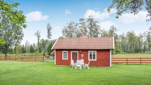 Una casa de madera roja con techo de tejas, patio cercado y una mesa con sillas afuera.