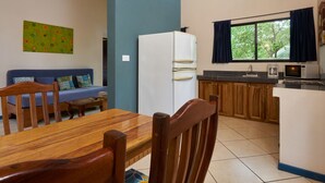 Une cuisine compacte équipée d’un réfrigérateur, d’un four à micro-ondes et d’un évier. Une table à manger avec des chaises se trouve au premier plan.