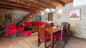 A cozy room with a stone wall, wooden ceiling, a red sofa, a dining table with chairs, and a staircase. - Amazing home in Ploce with sauna (Ploce)