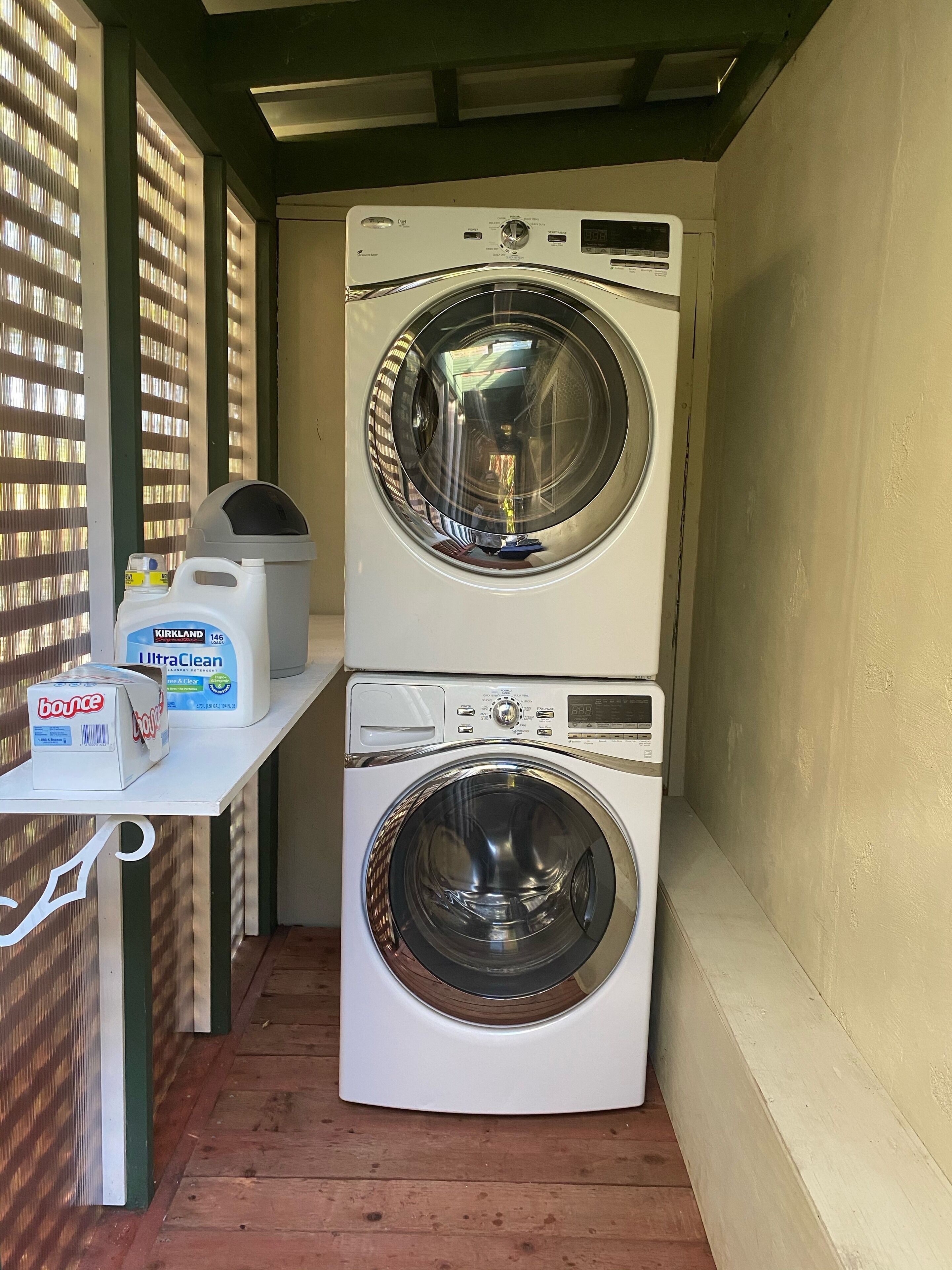 Un espace buanderie compact comprenant deux machines à laver à chargement frontal superposées et une table sur laquelle sont posées des bouteilles de lessive.