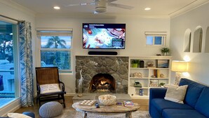 Ein Wohnzimmer mit Kamin aus Stein, einem darüber montierten Fernseher, einem blauen Sofa, einem Couchtisch und einem Bücherregal.