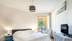 Quarto de hotel com cama, televisão, cadeira, mesa e varanda com vista para árvores.