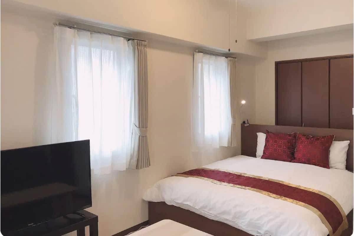 A hotel room with a bed, curtains, a television, and a ceiling fan.
