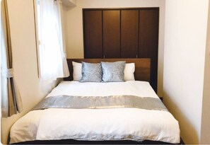 A neatly made bed with a wooden headboard, white bedding, and two decorative pillows. - Osaka Yodoyabashi House (Osaka)