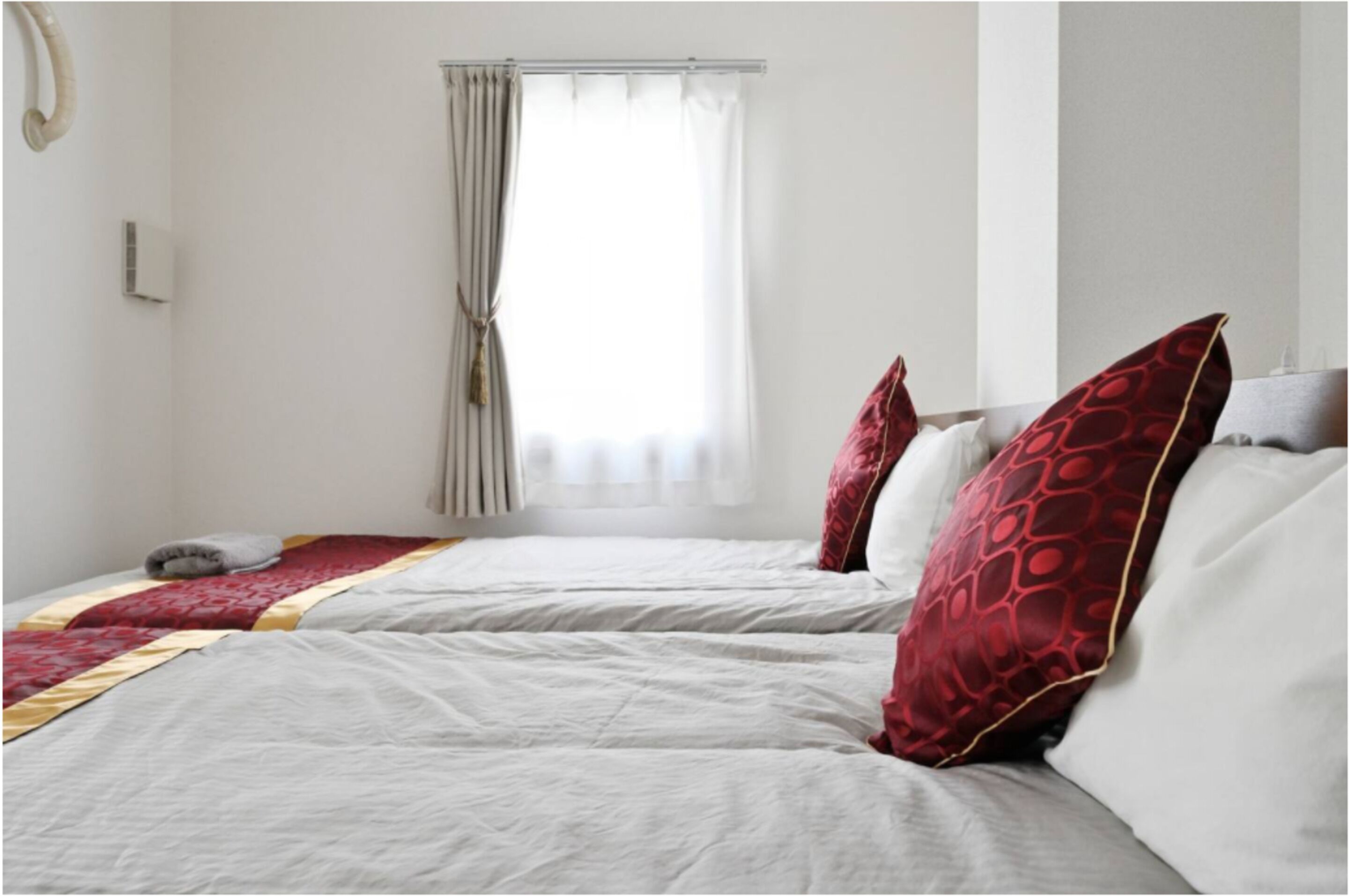 Ein Hotelzimmer mit zwei Betten, jedes mit einem roten, gemusterten Kissen, einer weißen Bettdecke und einem Fenster mit Vorhängen.