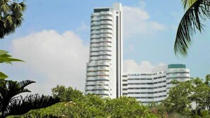 Ein modernes Hochhaus mit mehreren Balkonen, umgeben von üppiger Vegetation und Palmen.