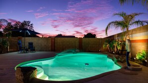 A swimming pool with a stone edge, surrounded by a brick wall and palm trees. - THE ONE!! Spa⁕Heated Pool⁕Fire Pit ⁕Putting Green  (Peoria)