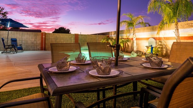An outdoor dining area with a pool table, chairs, and a table set for a meal. - THE ONE!! Spa⁕Heated Pool⁕Fire Pit ⁕Putting Green  (Peoria)