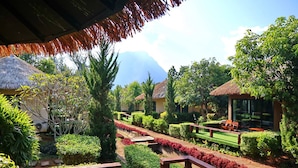 A well-maintained garden with neatly trimmed hedges, a pathway, and a thatched-roof structure. - The Breath Chiangdao (Chiang Dao)