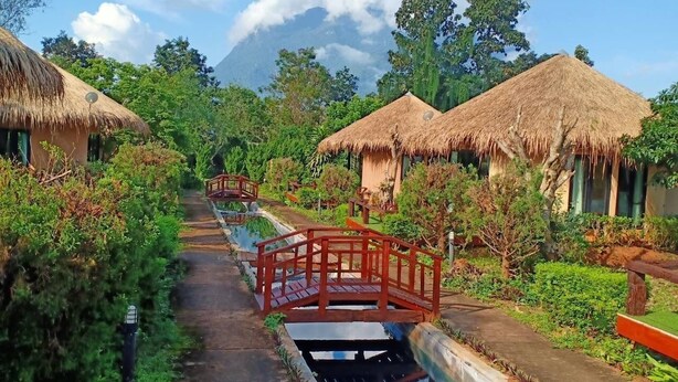 A pathway leading to thatched-roof huts with a small bridge over a water channel. - The Breath Chiangdao (Chiang Dao)