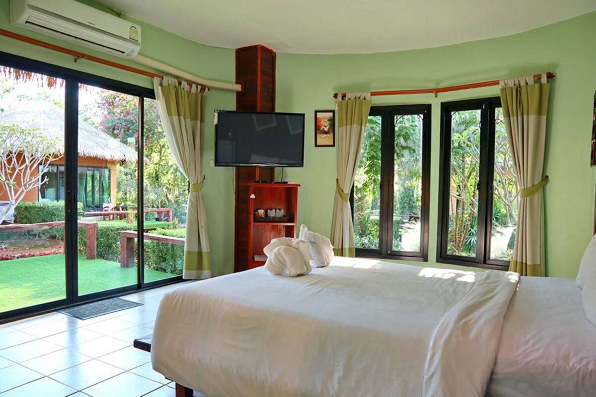 A hotel room with a large bed, a television, and a view of a garden through the sliding glass door.