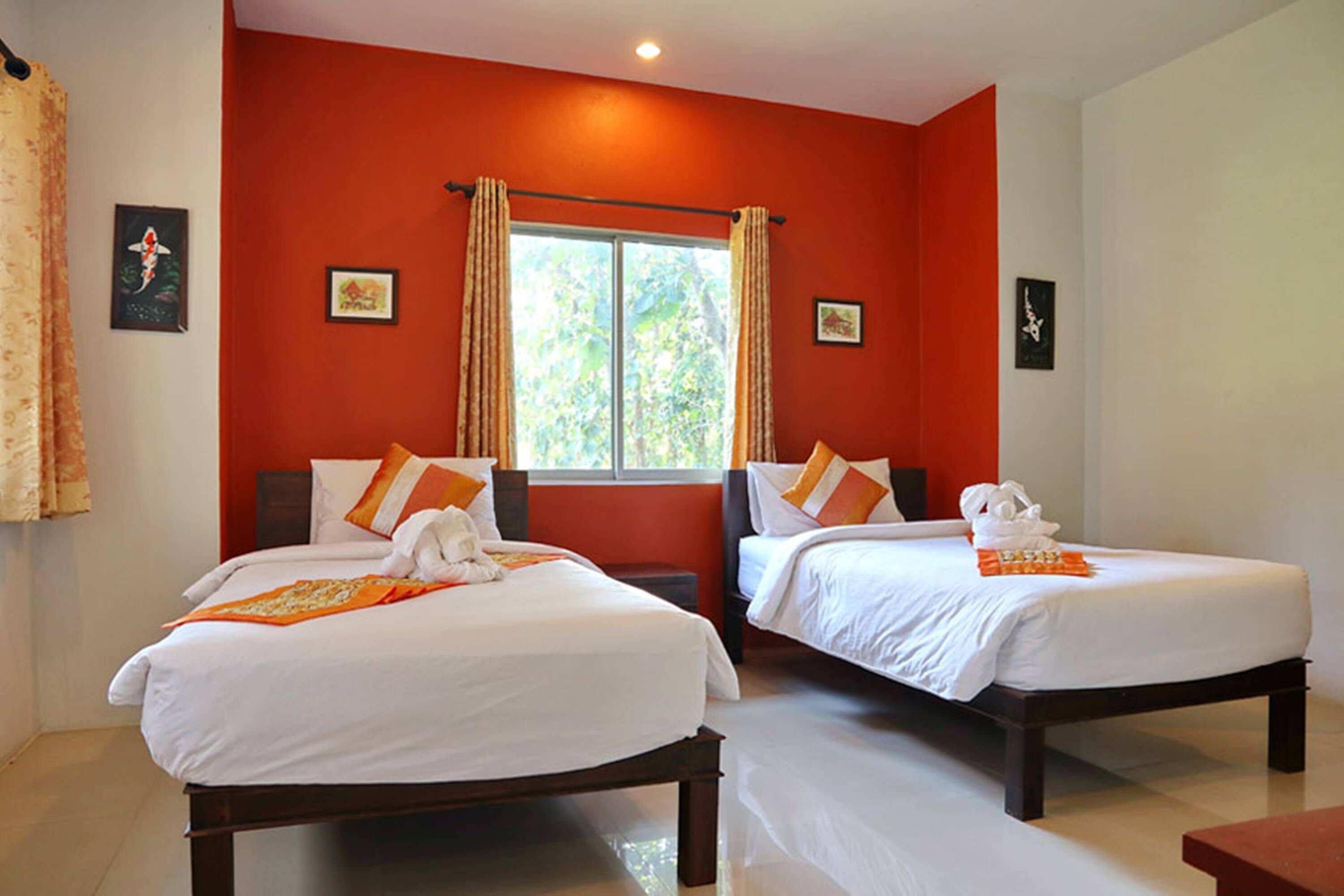 A hotel room with two beds, red walls, and a window with curtains.