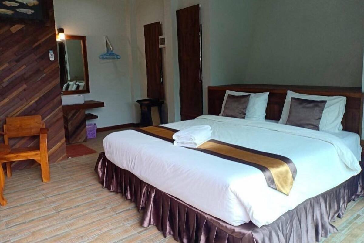 A hotel room with a large bed, a wooden chair, a desk, and a mirror.