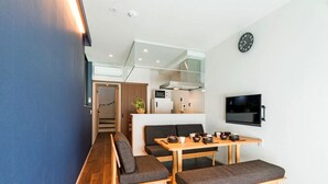 Um espaço de estar moderno com área de jantar, sofá, TV e cozinha ao fundo.