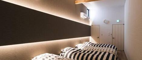 Una habitación estrecha, tenuemente iluminada, con techo inclinado, vigas de madera y una cama con ropa de cama a rayas.