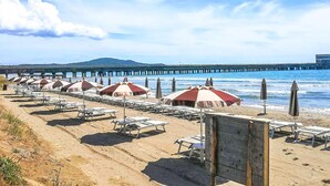 A beach with rows of sun loungers and umbrellas, a pier in the background, and a clear sky. - Stunning apartment in Puntone with WiFi (Puntone)