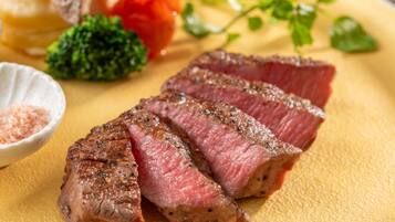 A plate of sliced steak with a side of vegetables and a small bowl of salt.